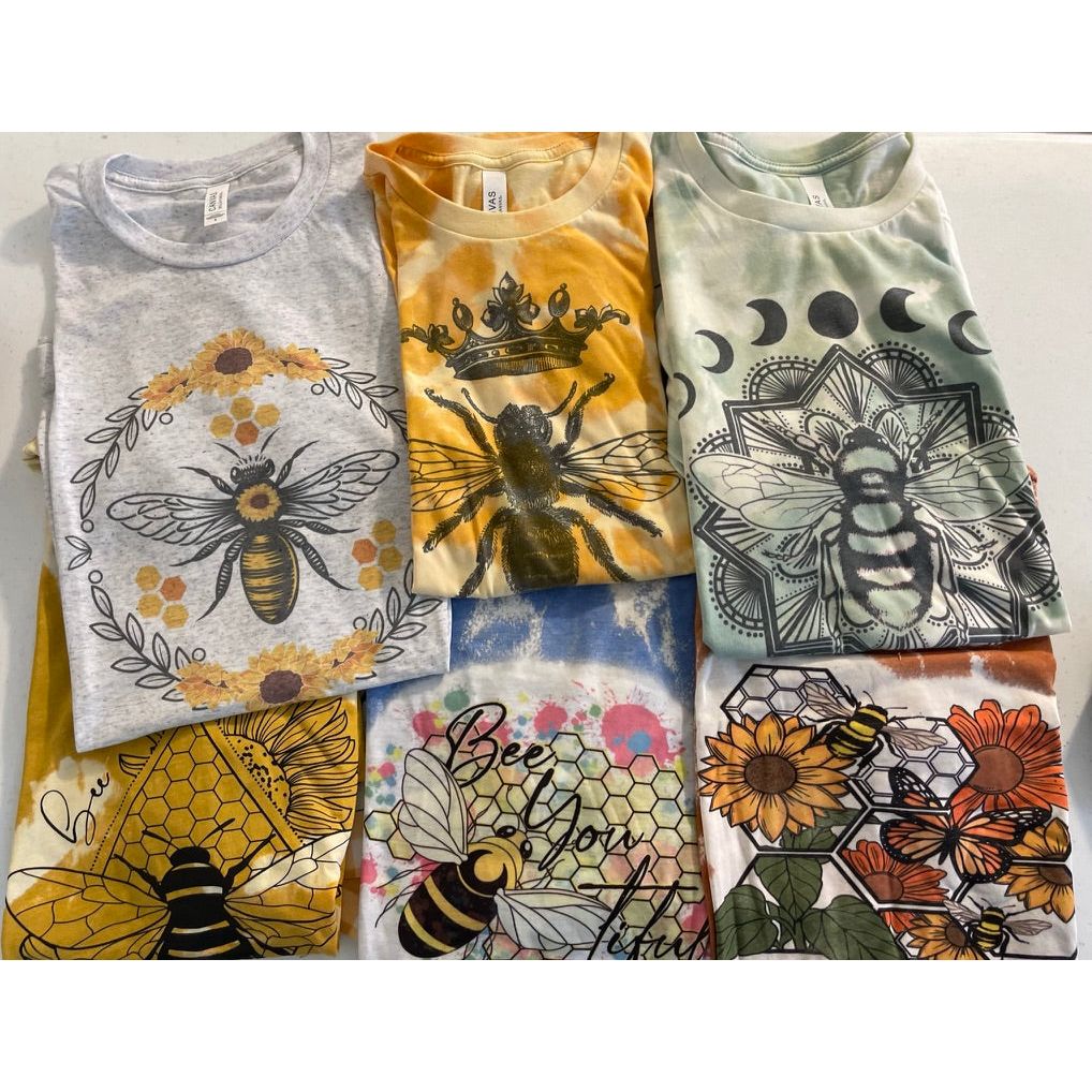 Honey Bee Circle T-Shirt and others folded for display of pollinator tee shirts.